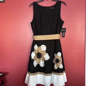 Black sleeveless dress with sash and flower trim.